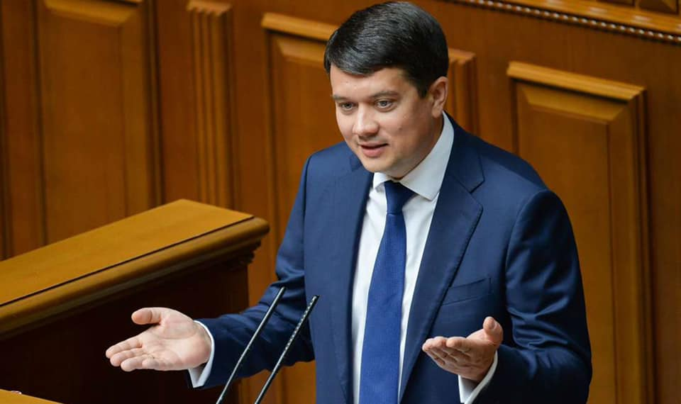 Чоловік виступає за трибуною в діловому костюмі.