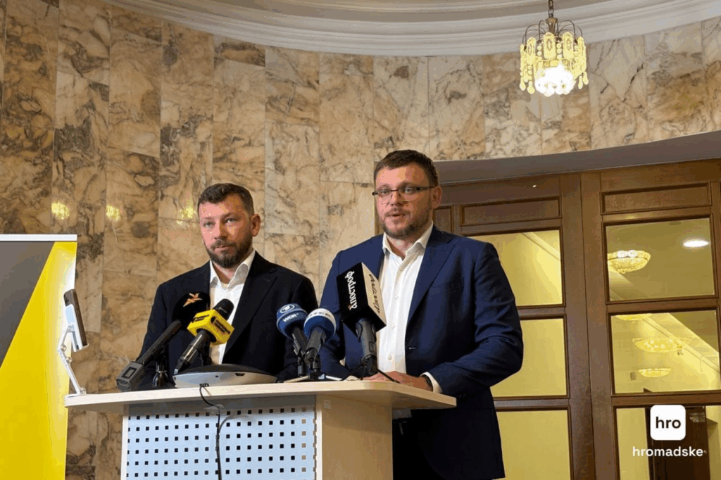 Двоє чоловіків на прес-конференції з мікрофонами
