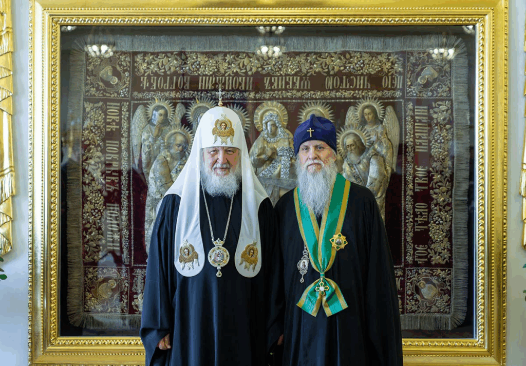 Два священнослужителі перед іконою в золотій рамі.