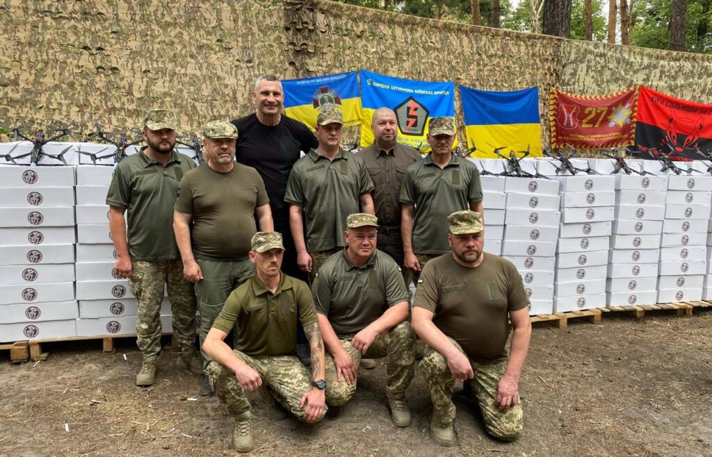 Групове фото військових перед прапорами та ящиками.