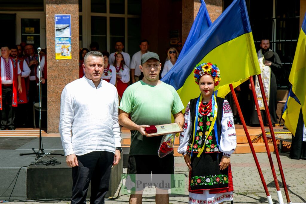Люди в національному вбранні біля українських прапорів.