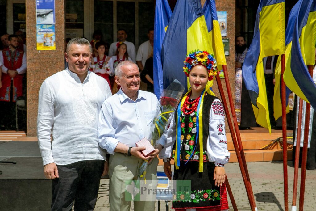 Люди в національному одязі біля українських прапорів.