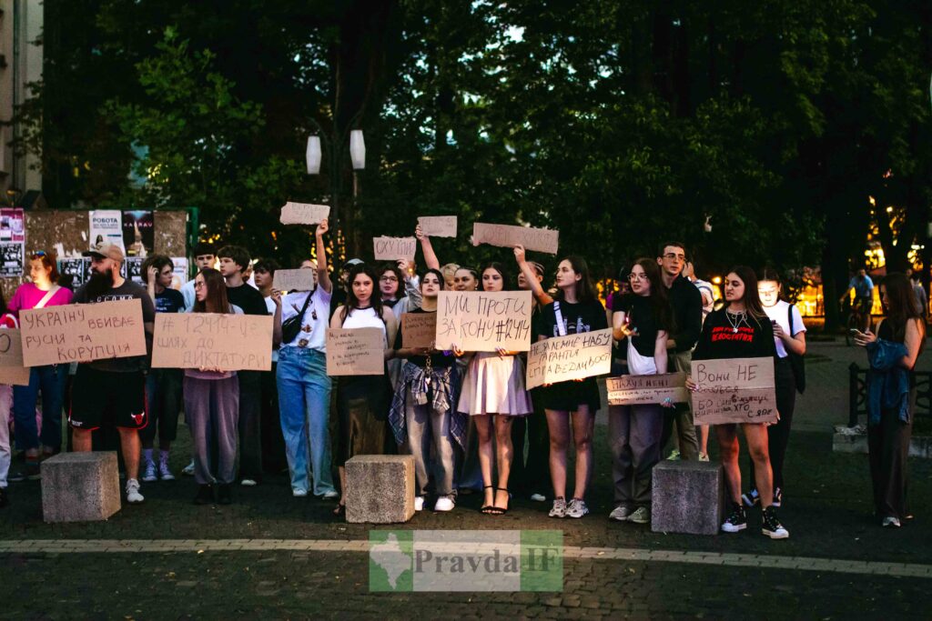 Люди тримають плакати на протесті вночі.
