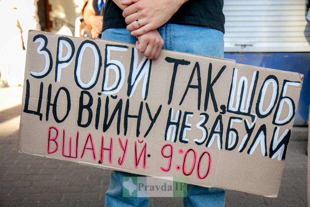 Людина тримає плакат з написом про війну.