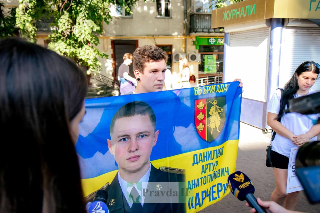 Люди тримають прапор з портретом військового героя.