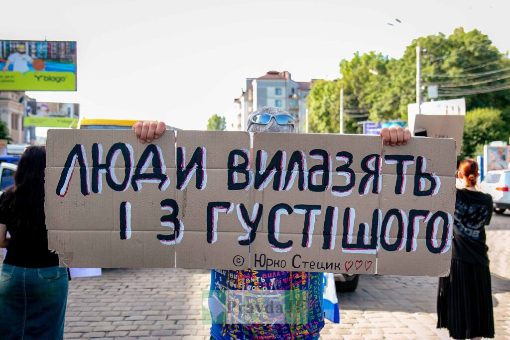 Протестувальник тримає плакат із написом українською.