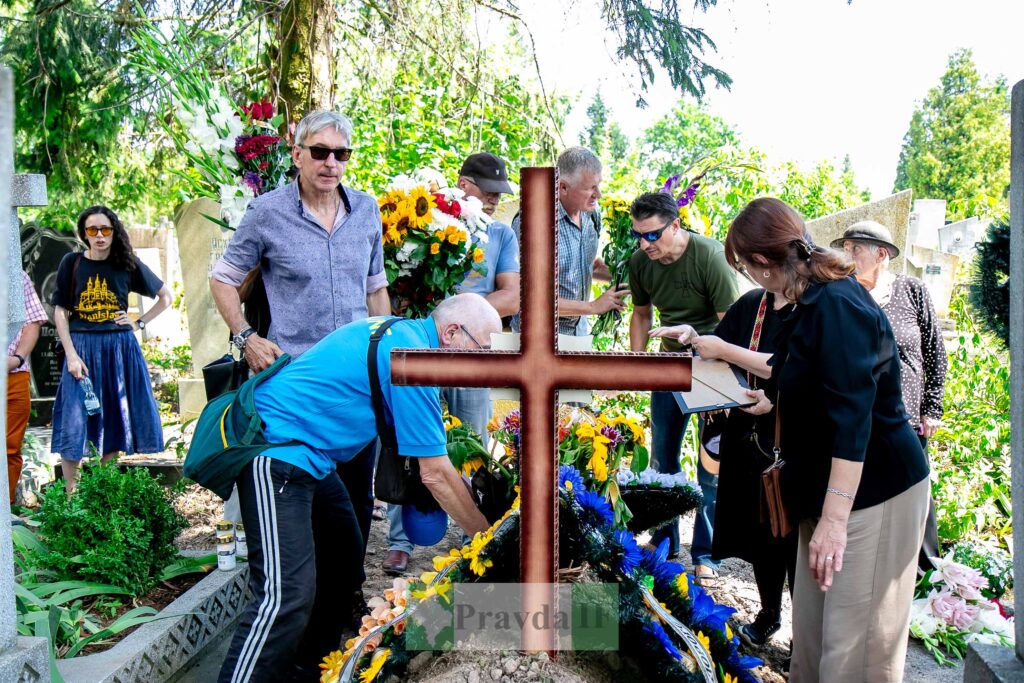 Люди з квітами біля могили на кладовищі.