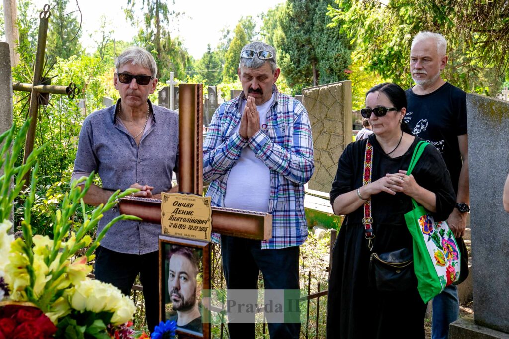 Люди біля могили на кладовищі, квіти на хресті