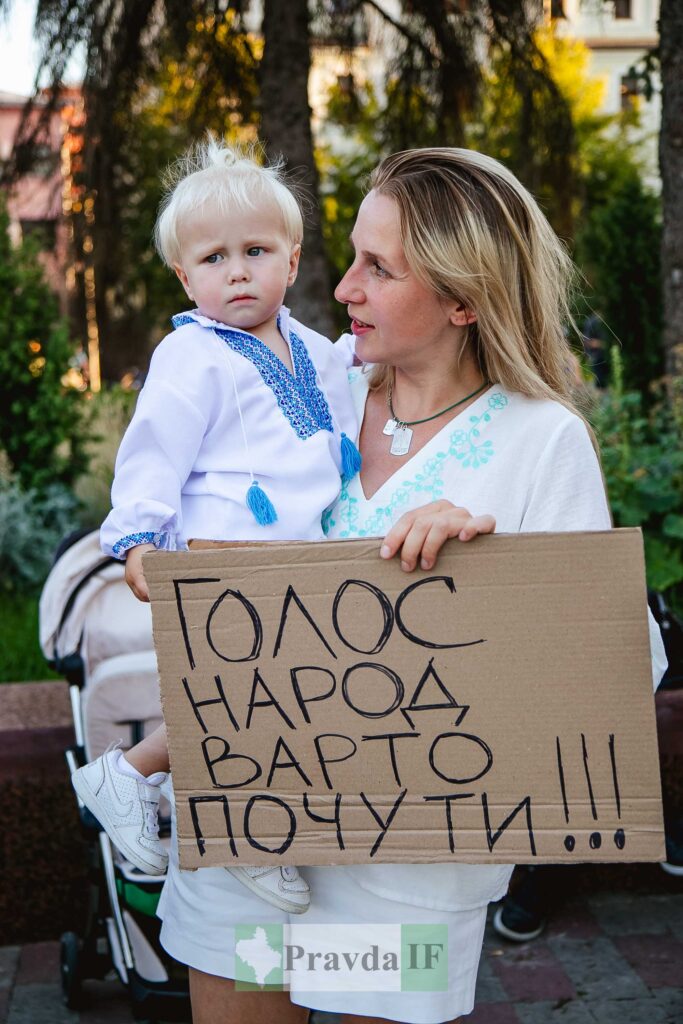 Жінка тримає дитину та напис на картоні.