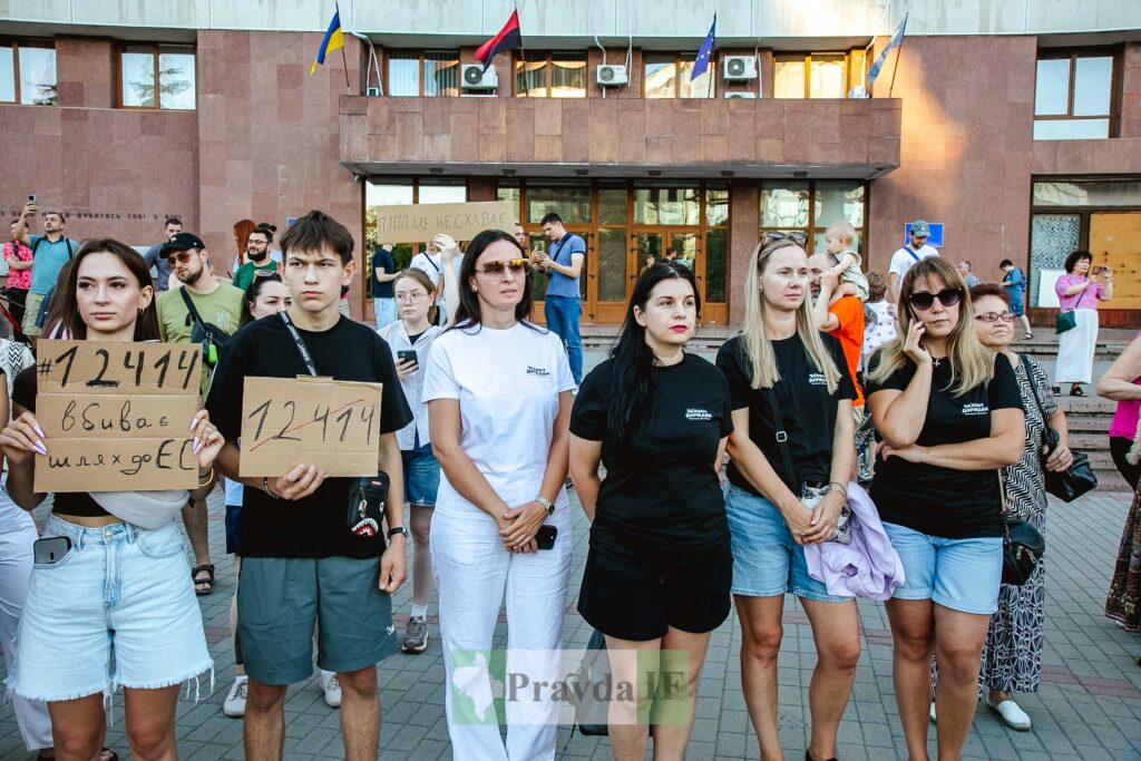 Люди тримають плакати на протесті перед будівлею.