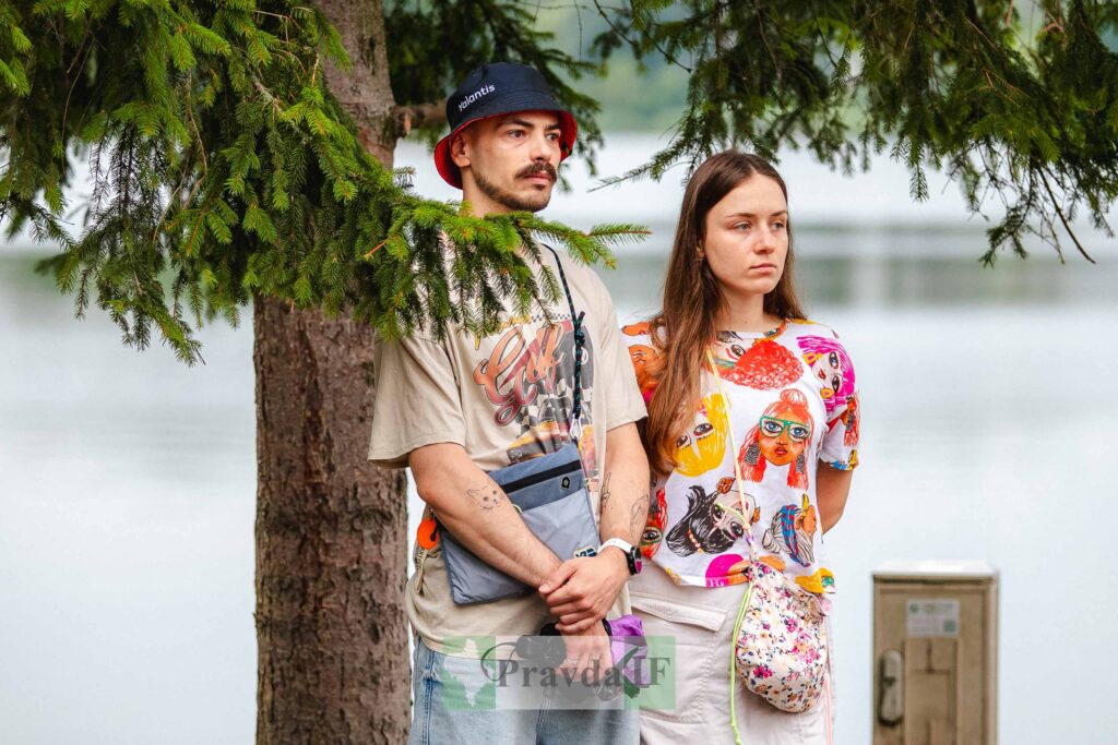 Люди стоять під деревом біля озера.