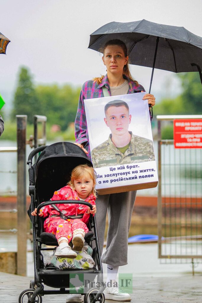 Жінка з плакатом, дитина в колясці, під парасолькою