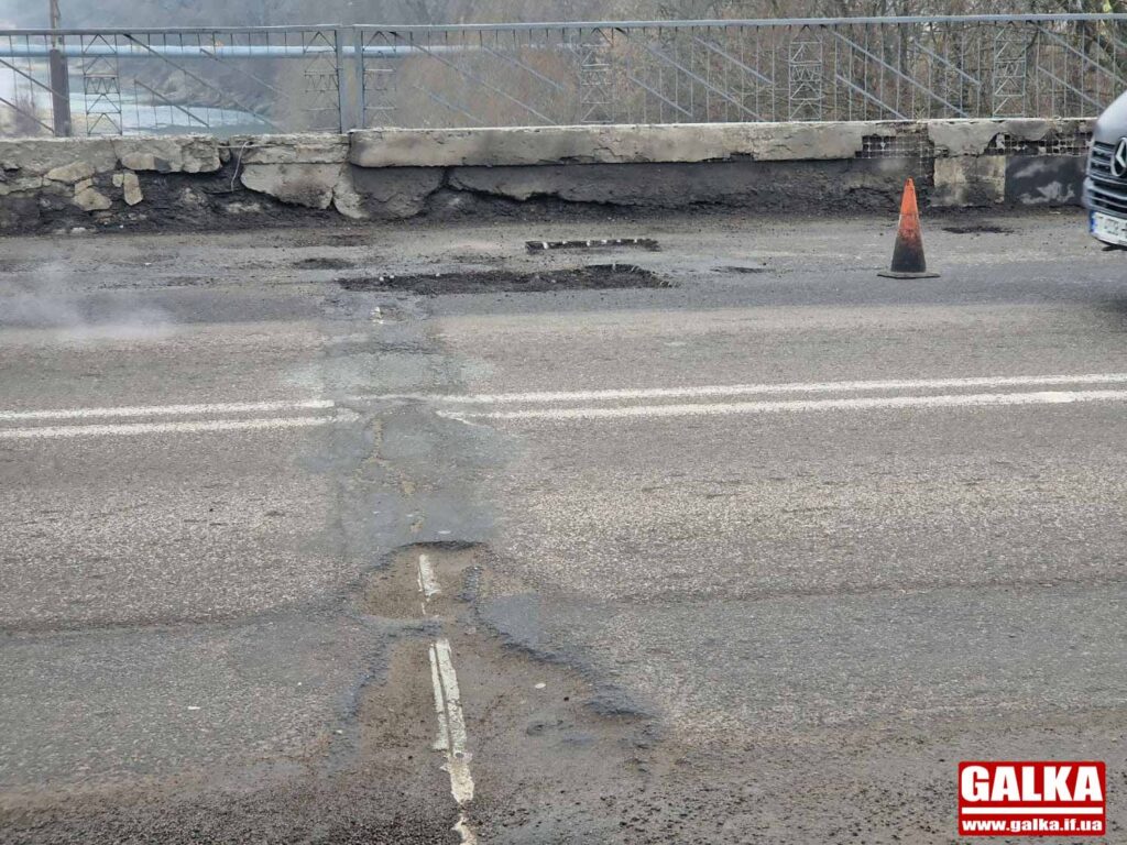 Пошкоджена дорога з ямами і безпековим конусом.