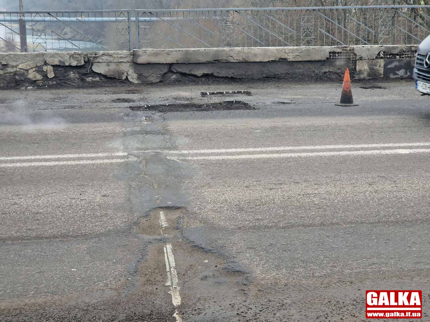 Пошкоджена дорога з ямами і безпековим конусом.