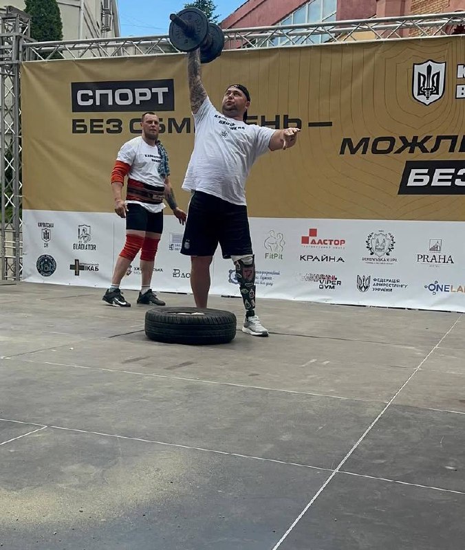 Спортсмен піднімає гантелю на відкритій сцені.