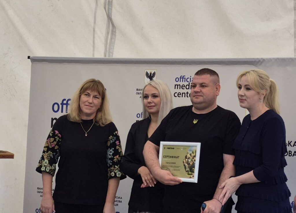 Люди тримають сертифікат біля банера медцентру.
