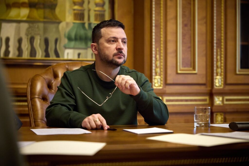 Чоловік у зеленому одязі за столом з документами.