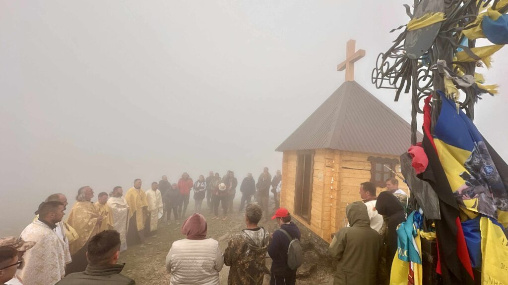 Церемонія біля дерев'яної каплиці в тумані на горі.