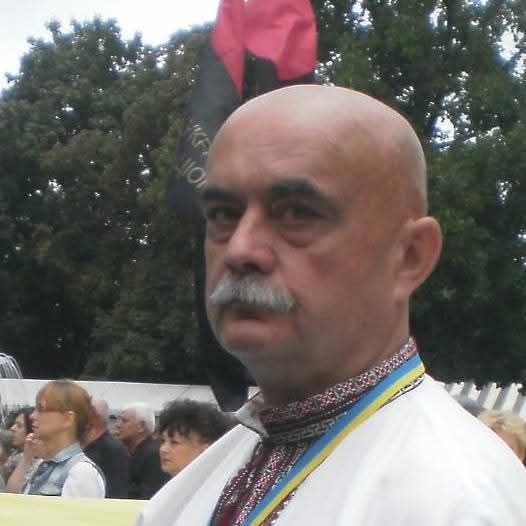 Людина в вишиванці на вулиці, прапор на фоні.