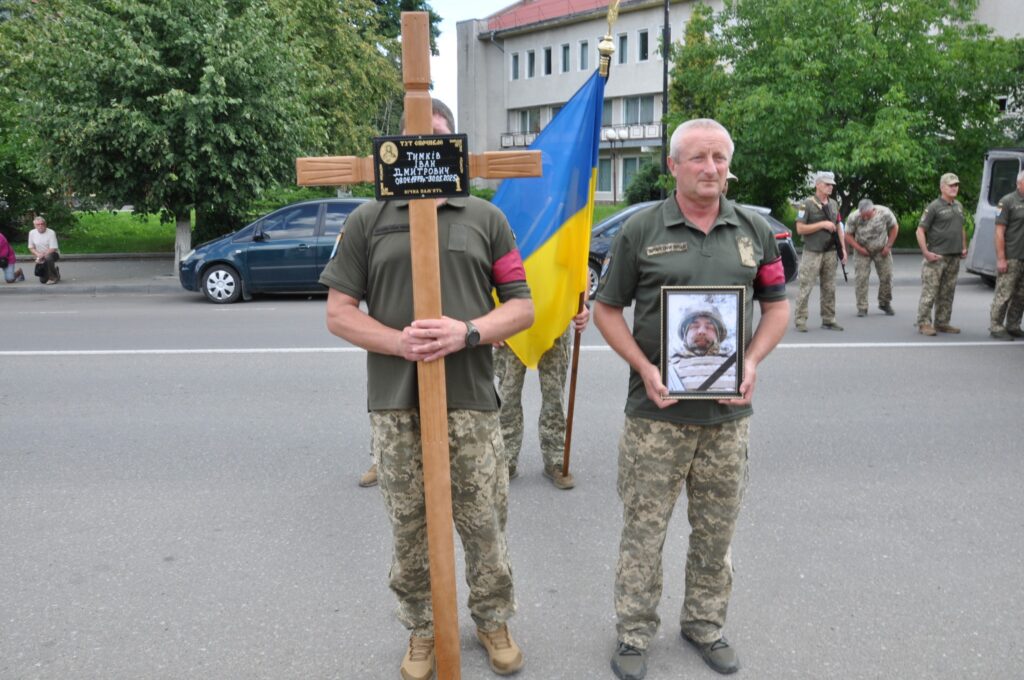 Українські військові тримають хрест і портрет солдата.