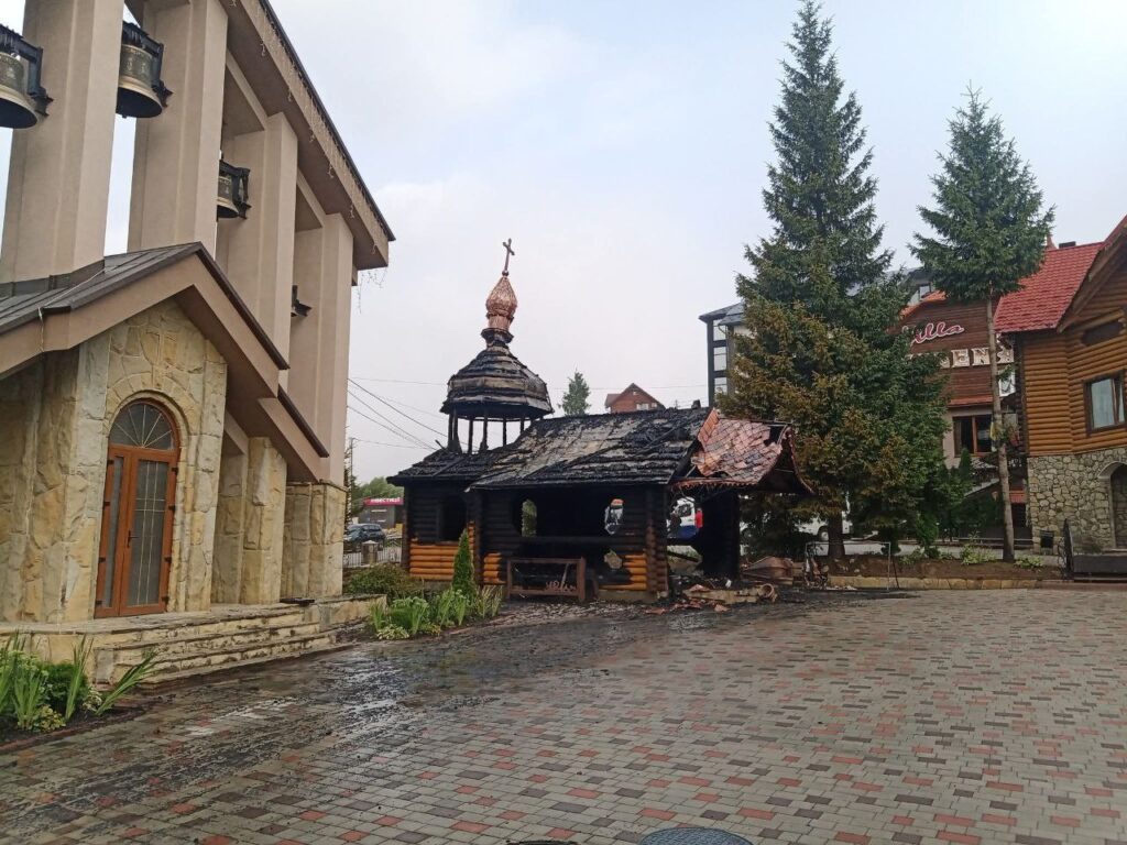 Згоріла дерев'яна будівля біля церкви, зелена ялина.