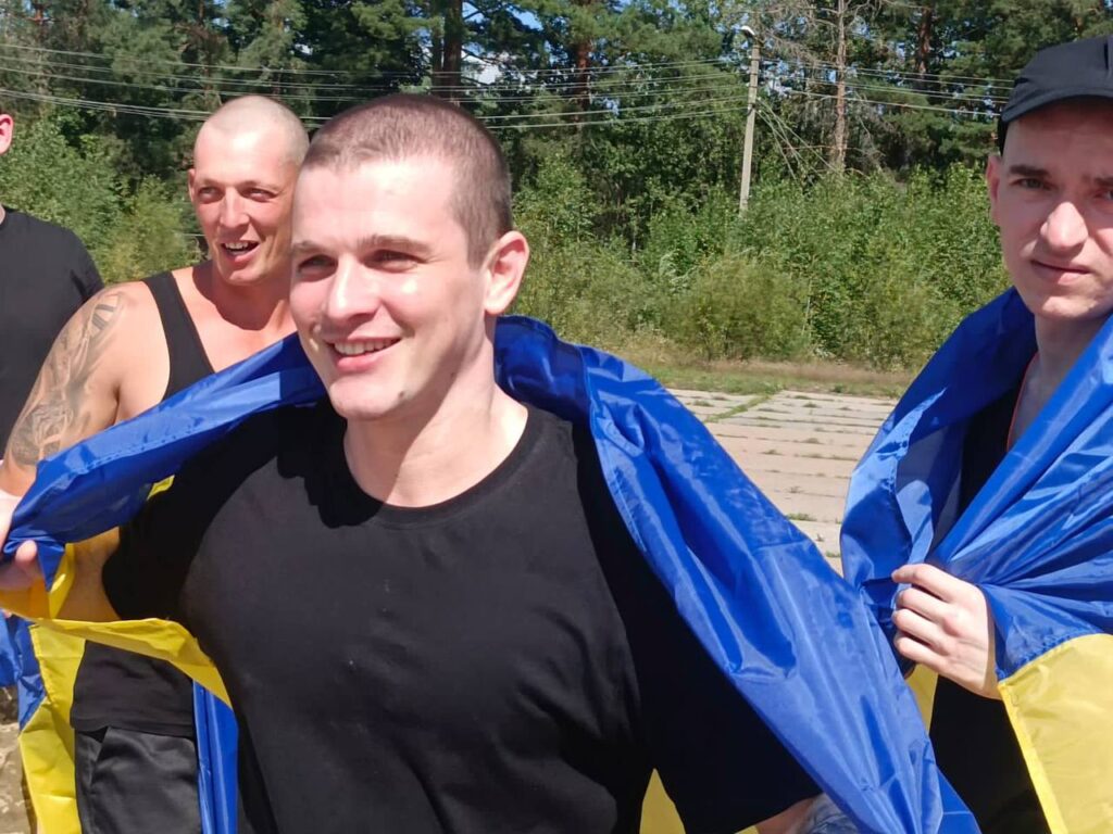 Люди з українським прапором на природі, радісні обличчя.
