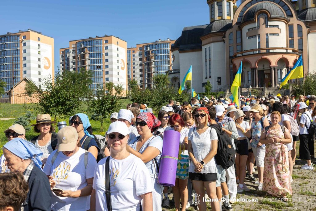 Люди на вулиці з українськими прапорами біля церкви.