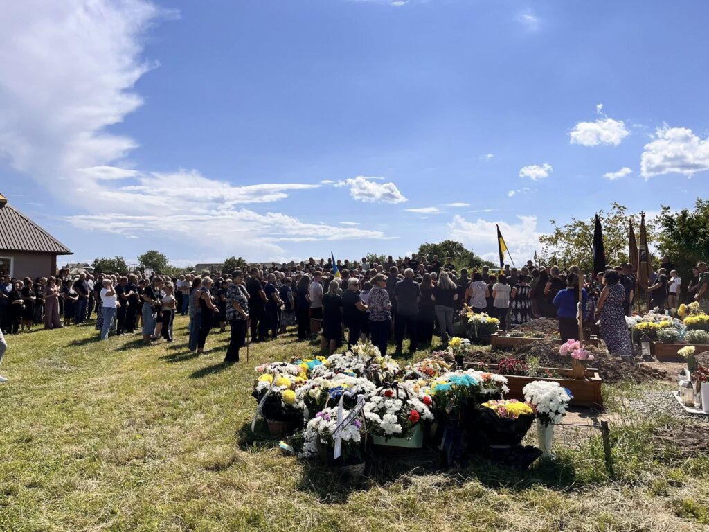 Люди зібрались на кладовищі, квіти на могилах.