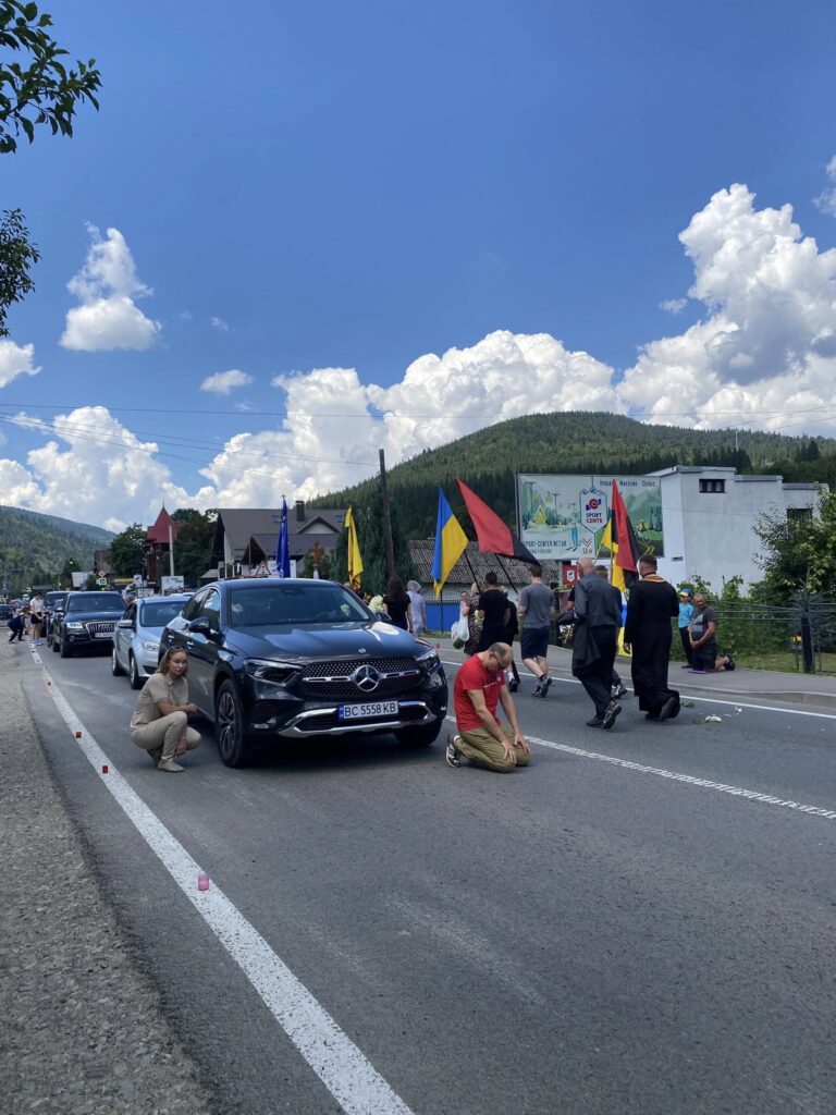 Вулична процесія з автомобілями та прапорами.