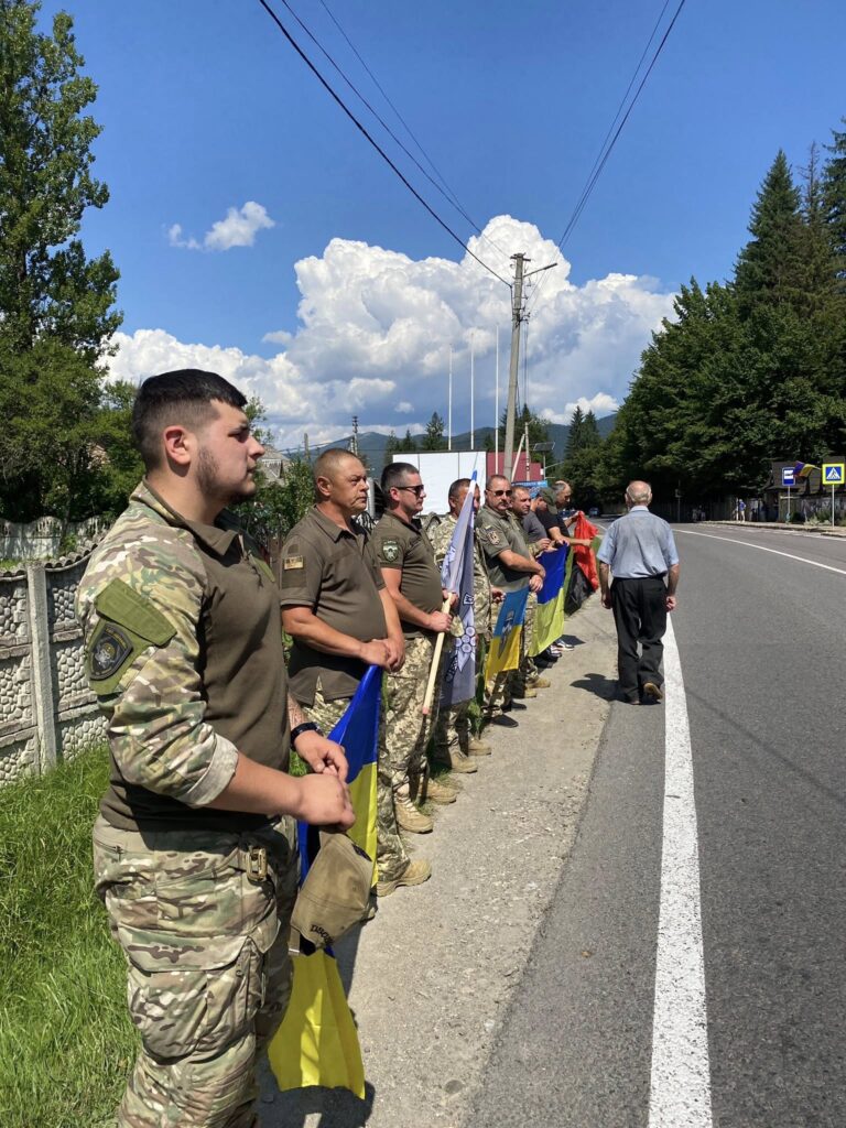 Військові стоять з прапорами біля дороги.