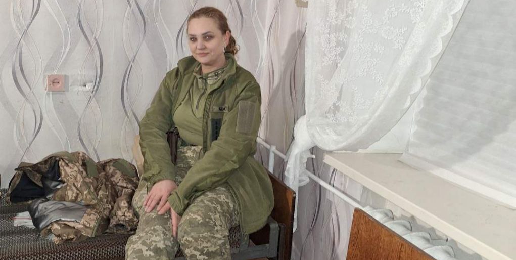 Жінка у військовій формі сидить у кімнаті.