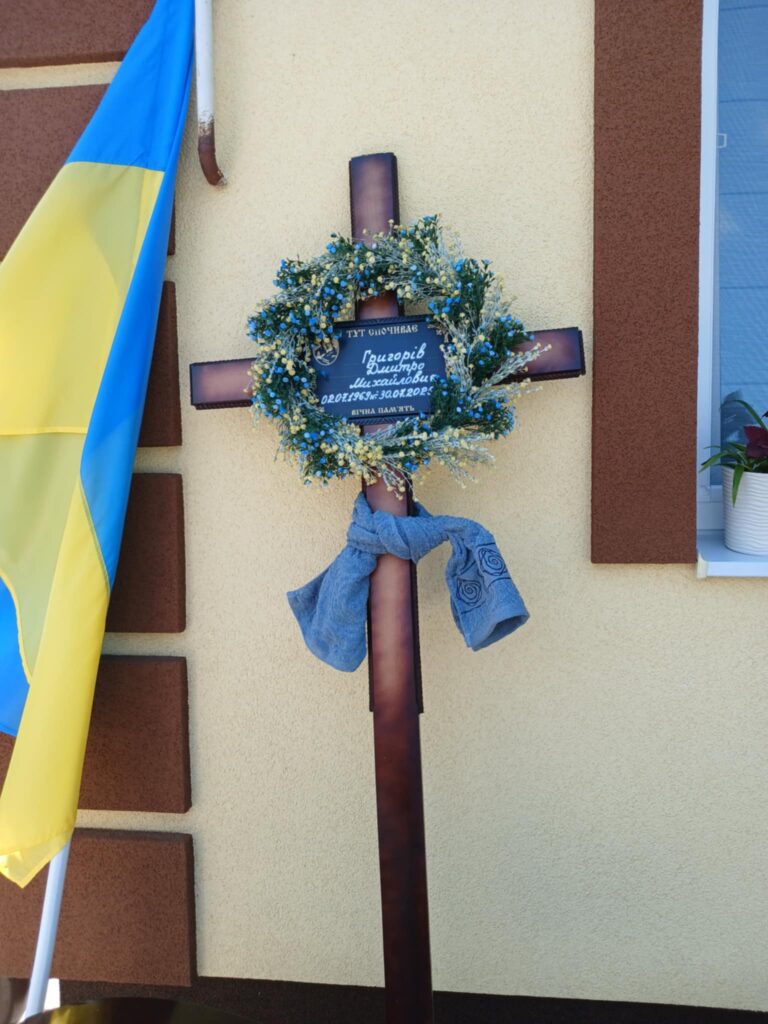 Хрест з вінком біля українського прапора.