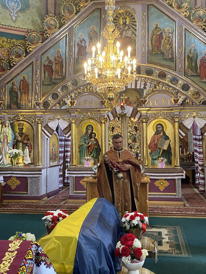 Священик в церкві біля труни, декор з квітів.