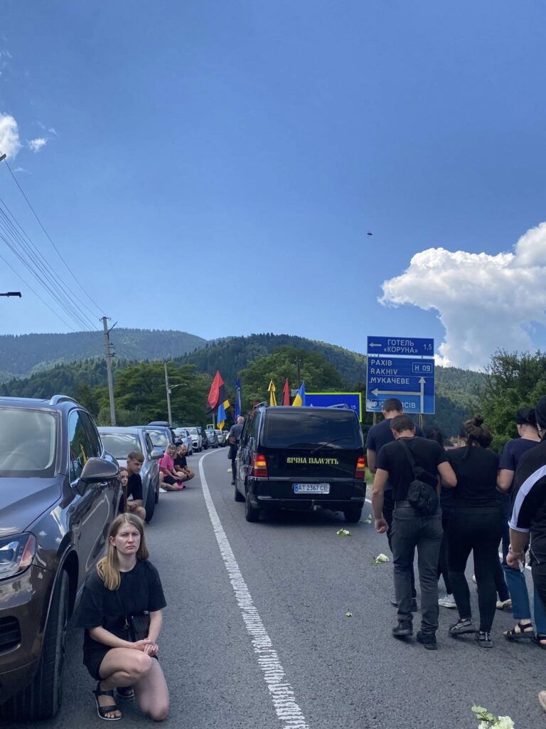 Люди на дорозі з автомобілями і прапорами.