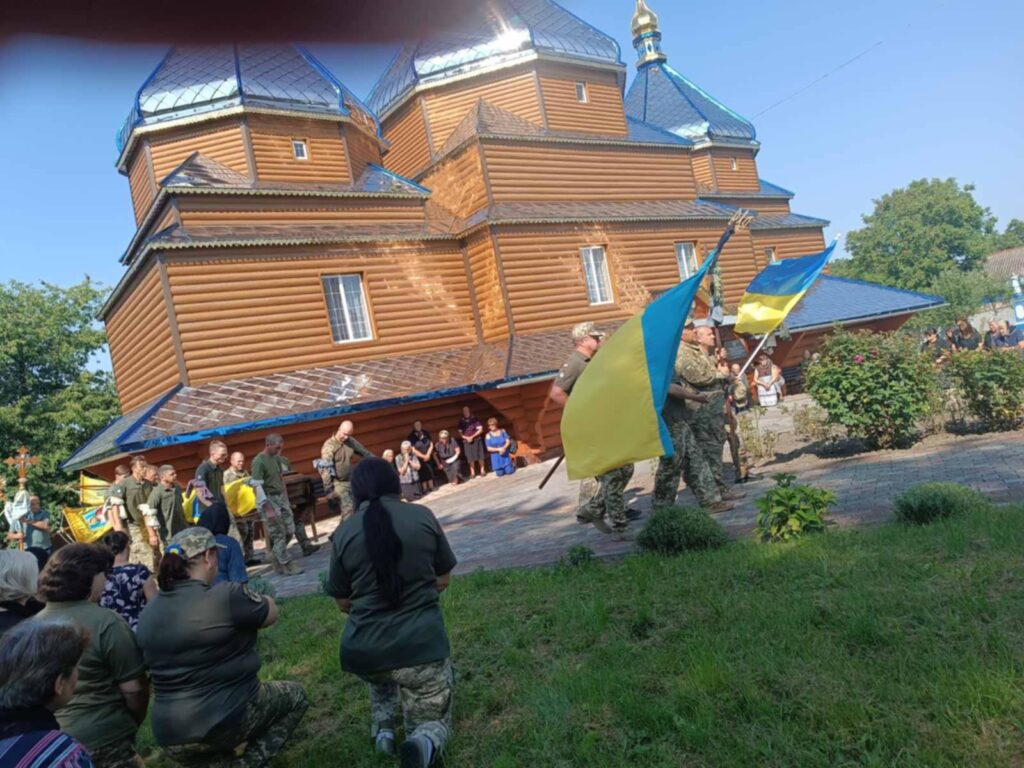 Військові з прапорами біля дерев'яної церкви, Україна