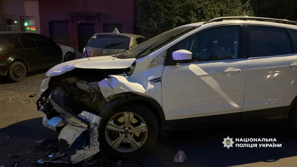 Пошкоджений білий автомобіль після аварії вночі.
