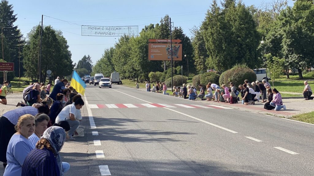 Люди на колінах вздовж дороги з прапором України.