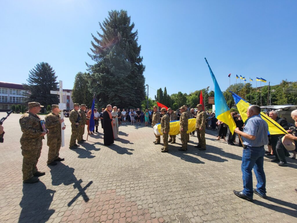Похоронна процесія з українським прапором на вулиці.