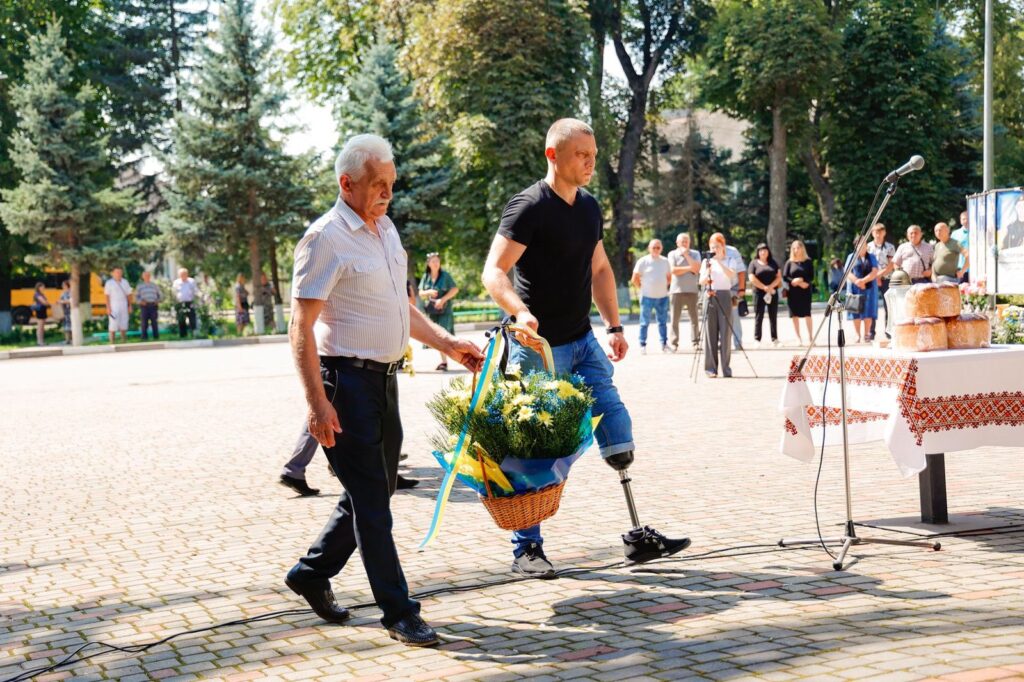 Двоє чоловіків несуть кошик квітів до столу.