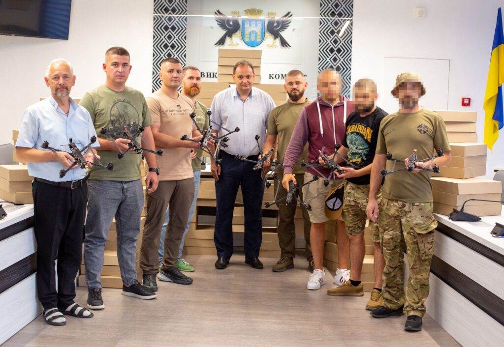 Група людей з дронами в приміщенні, прапор України.