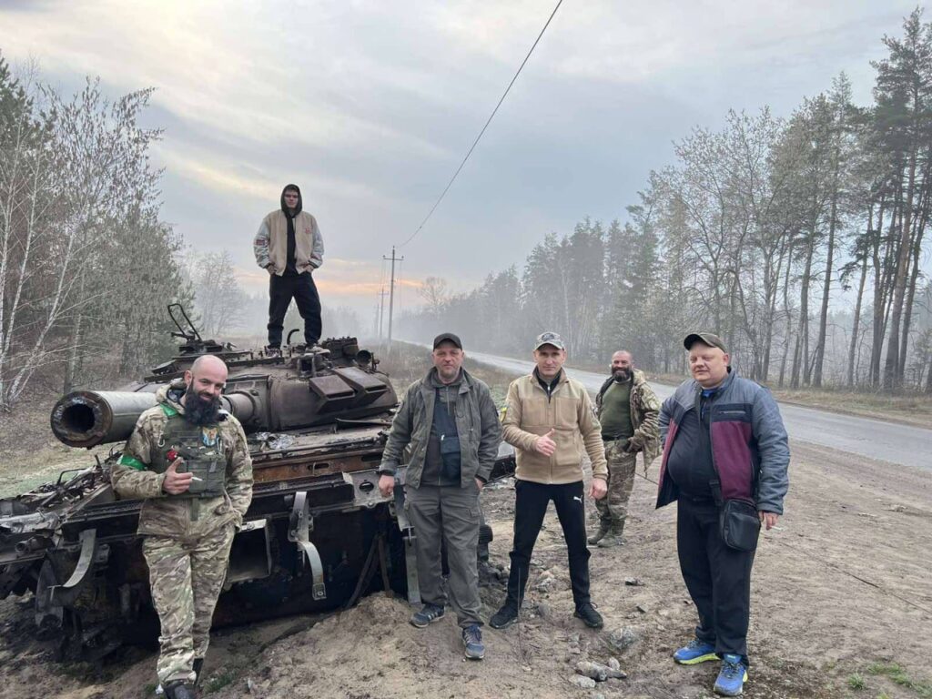 Люди стоять біля старого танка на дорозі.