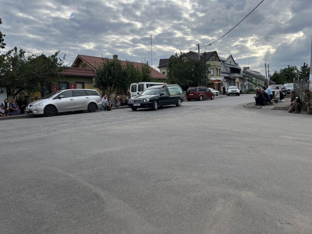 Люди сидять на вулиці біля автомобілів.
