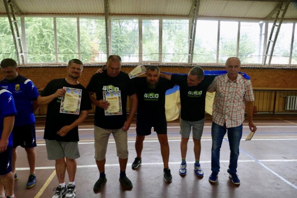 Група чоловіків тримає грамоти в спортивному залі.