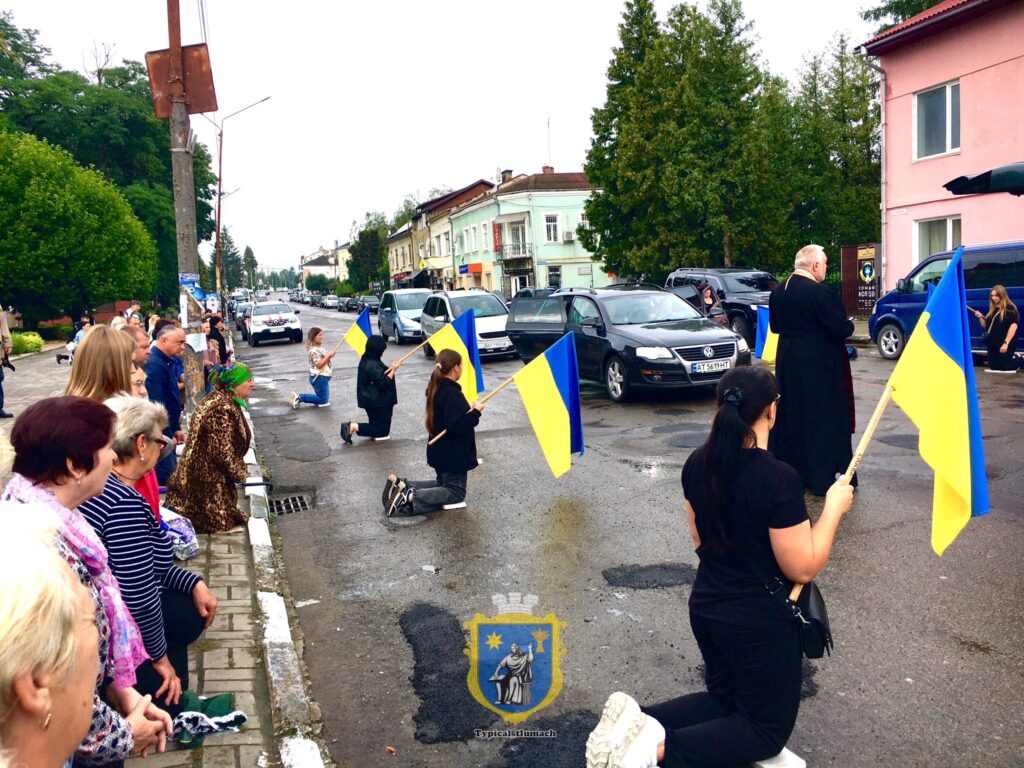 Люди на колінах із прапорами України на вулиці.