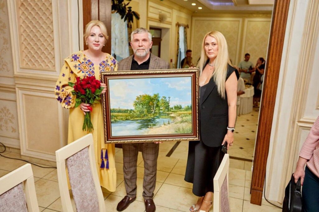 Три людини тримають мальовничий пейзаж з річкою.
