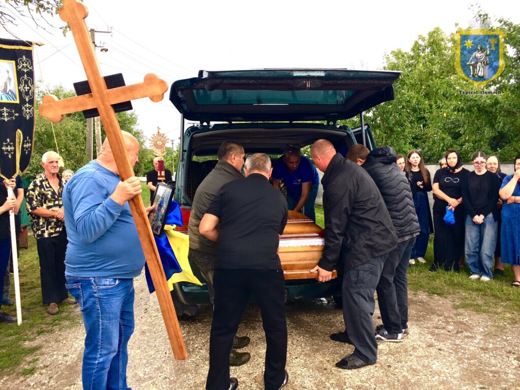 Похоронна процесія: труна, хрест і люди навколо.