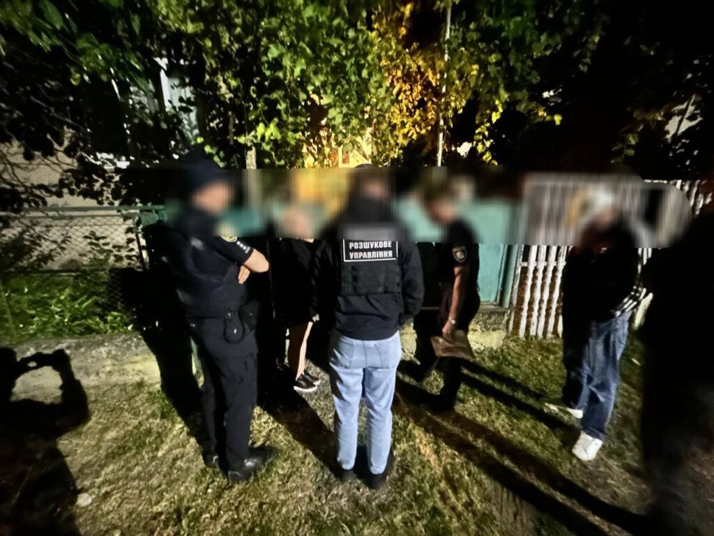 Група людей обговорює щось на вулиці вночі.
