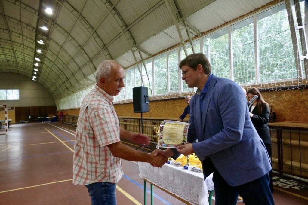 Чоловік вручає грамоту іншому чоловіку у залі