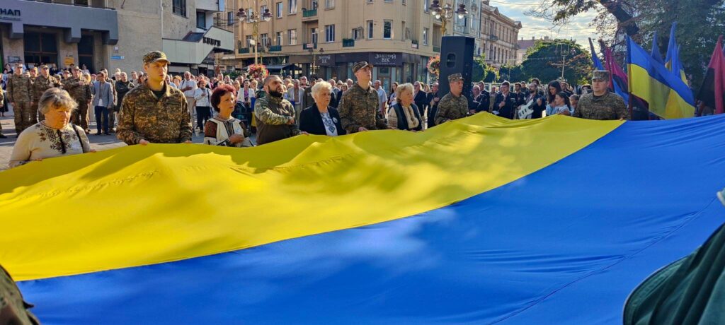 Люди тримають великий український прапор на вулиці.