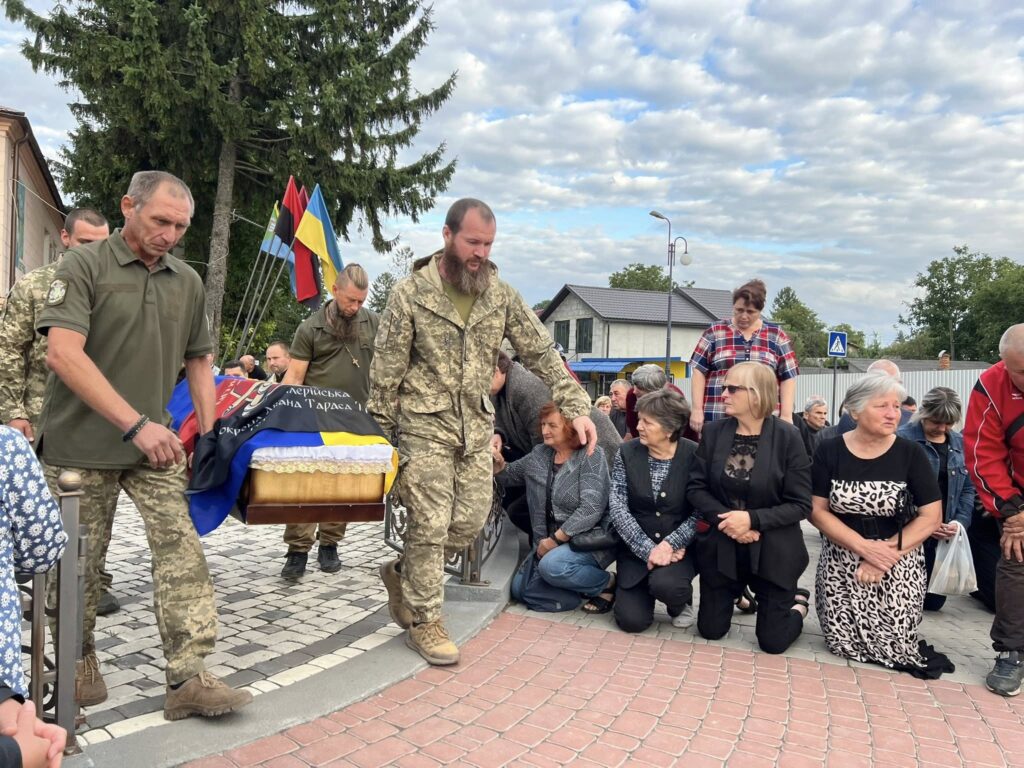 Церемонія похорону з військовими та людьми на колінах.